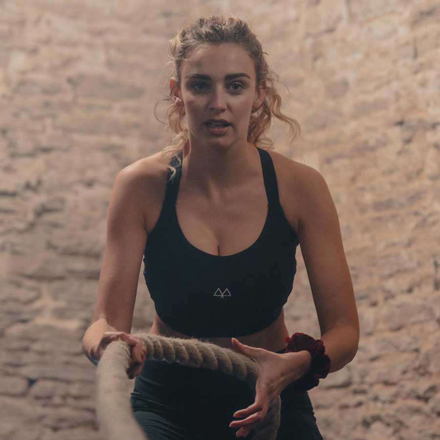 Izzy working out in the Gym doing Rope Pulls, wearing the Black MAAREE High-Impact Sports Bra, with a Red Scrunchies on her wrist.